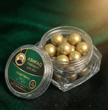 ASHFAQ Hakeem herbal tablets in a clear jar with gold-coated balls on a dark green fabric